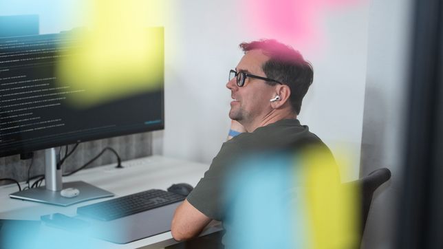 Ein Kollege mit Brille sitzt am Monitor, im Vordergrund unscharf bunte Haftnotizen.