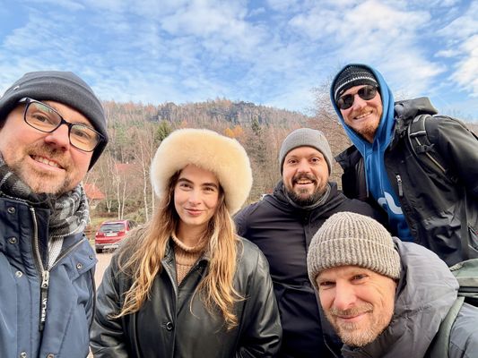 Selfie von fünf aus dem Team in Wintermützen, dahinter ein bewaldeter Berg mit Felsen.