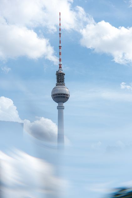 Der Berliner Fernsehturm über Wolken, davor eine unscharfe Glasfläche.