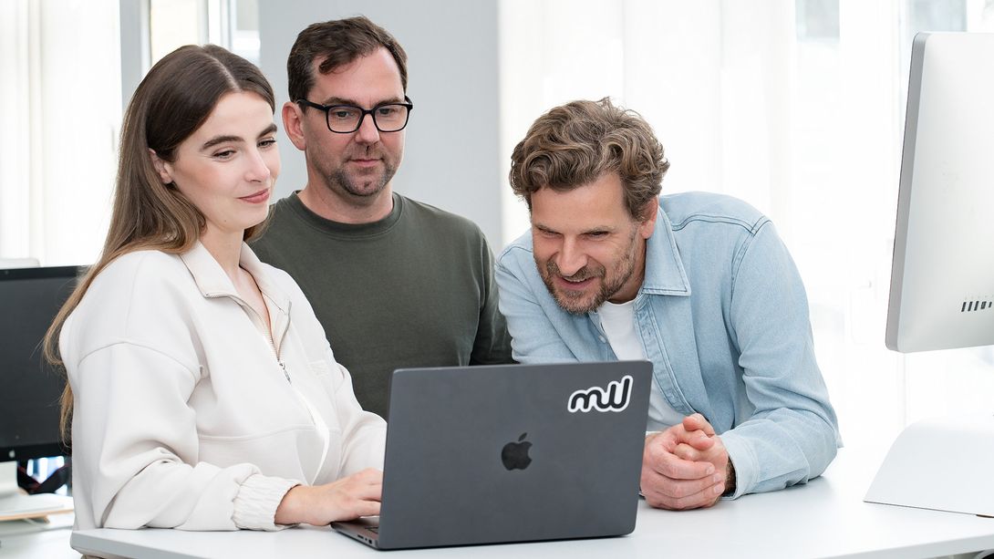 Drei Mitglieder des Teams schauen gemeinsam auf einen Laptop.
