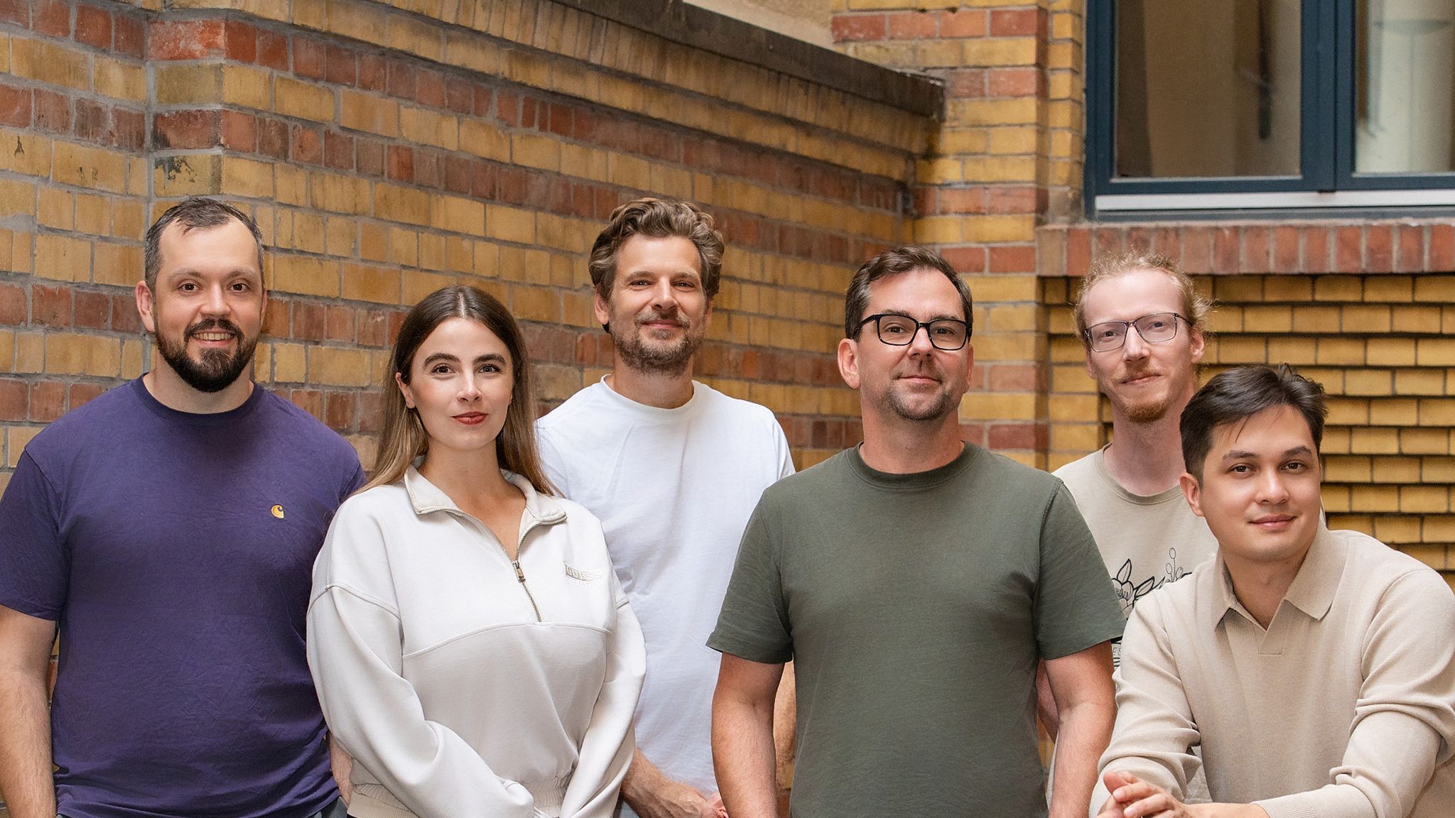 Sechs aus dem Team stehen nebeneinander vor einer Backsteinwand im Hof.